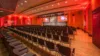 Rot beleuchteter Saal, mit Bühne und leeren Reihen