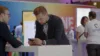 Mann lehnt auf einem Tisch. Er schaut aufs Handy. Er befindet sich auf einer Messe.