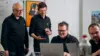 Vier Männer gucken auf einen Laptop. Sie lachen.